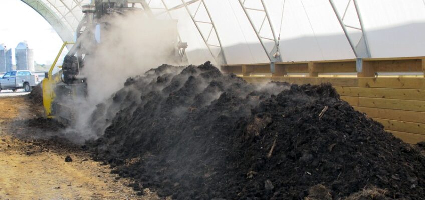 a row of covered compost being turned by a machine